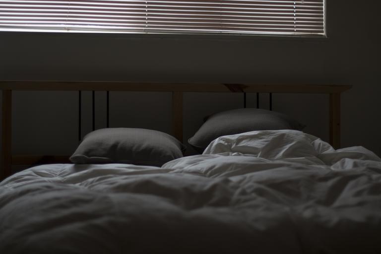 Spálňa so zatiahnutými žalúziami, posteľ s bielymi obliečkami a vankúšmi
